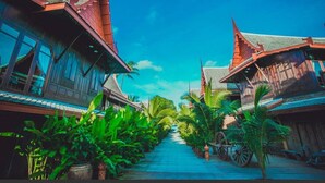 A traditional wooden building with a sloped roof and large windows, surrounded by lush greenery and a clear blue sky. - Sasitara   Thai  villas (Koh Samui)