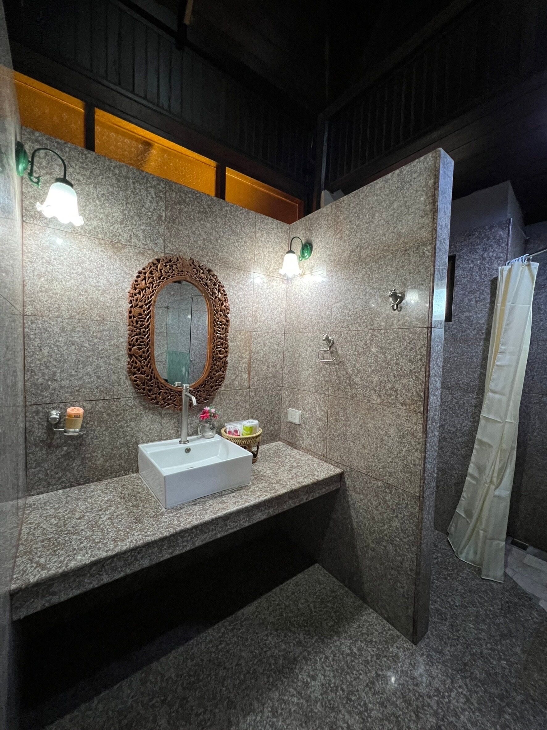 A modern bathroom with a granite countertop, a white sink, a decorative mirror, and a shower curtain.