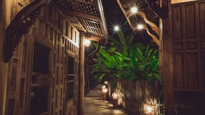 A narrow corridor with wooden architecture, illuminated by hanging lights and featuring a large plant. - Sasitara   Thai  villas (Koh Samui)