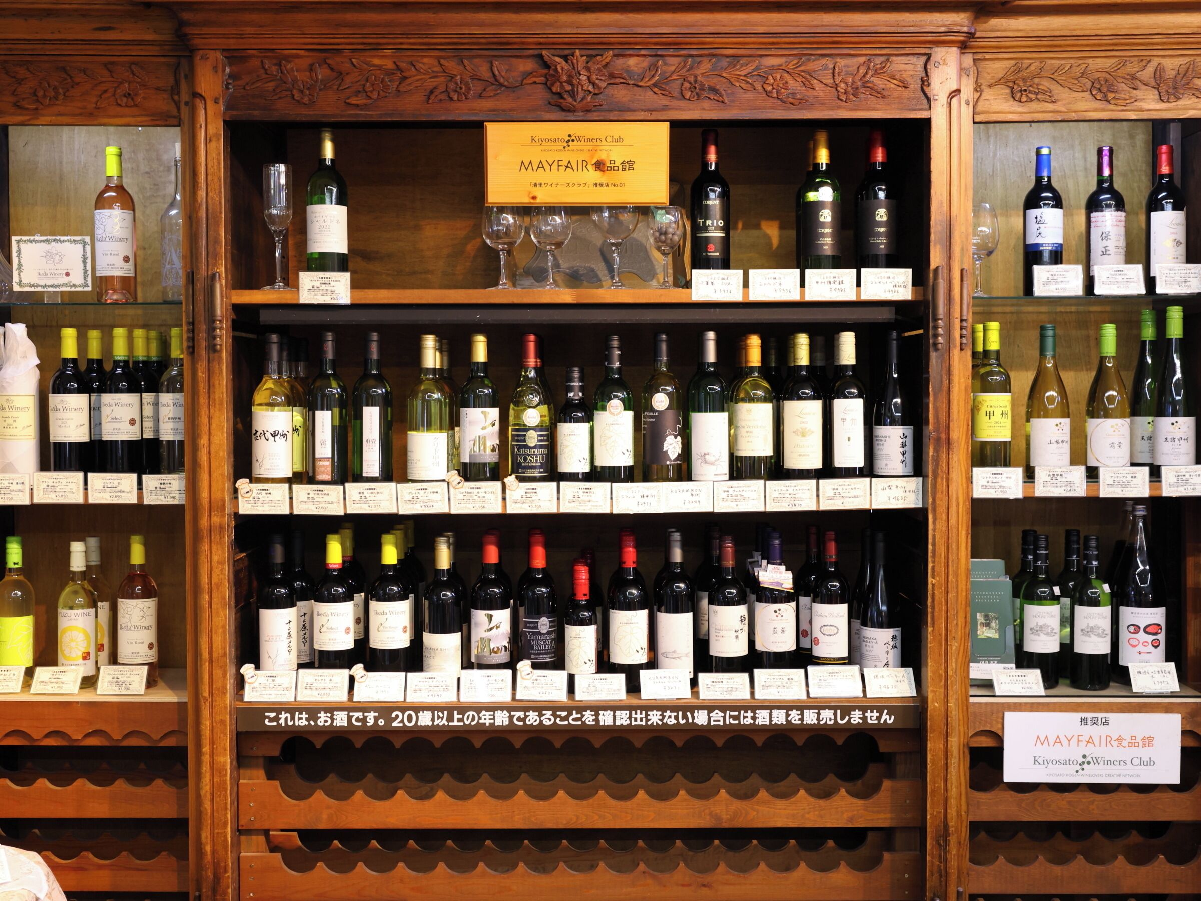 Eine Weinauslage mit verschiedenen Flaschen und Gläsern, inklusive eines Schildes für den Kiyosato Wine Club.
