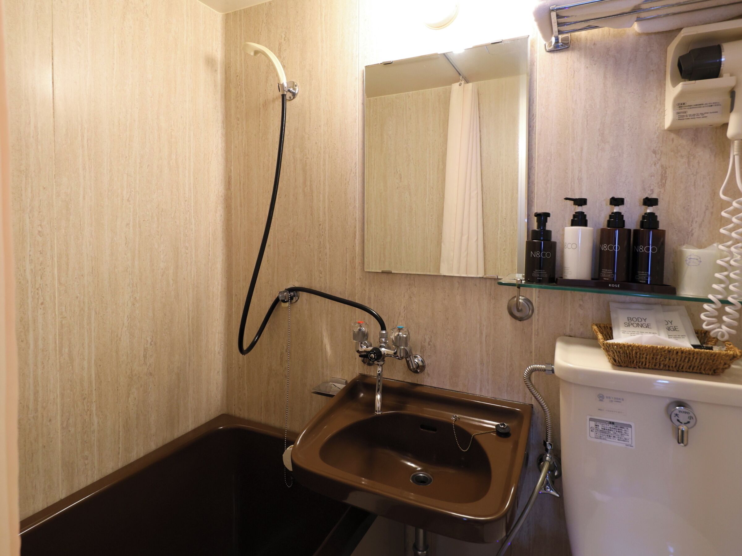 Een badkamer met een badkuip, een wastafel en een spiegel. Toiletartikelen staan op een plank.