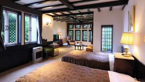 Habitación con dos camas, un escritorio, una silla y un televisor. Cuenta con ventanas amplias y un techo con vigas a la vista.