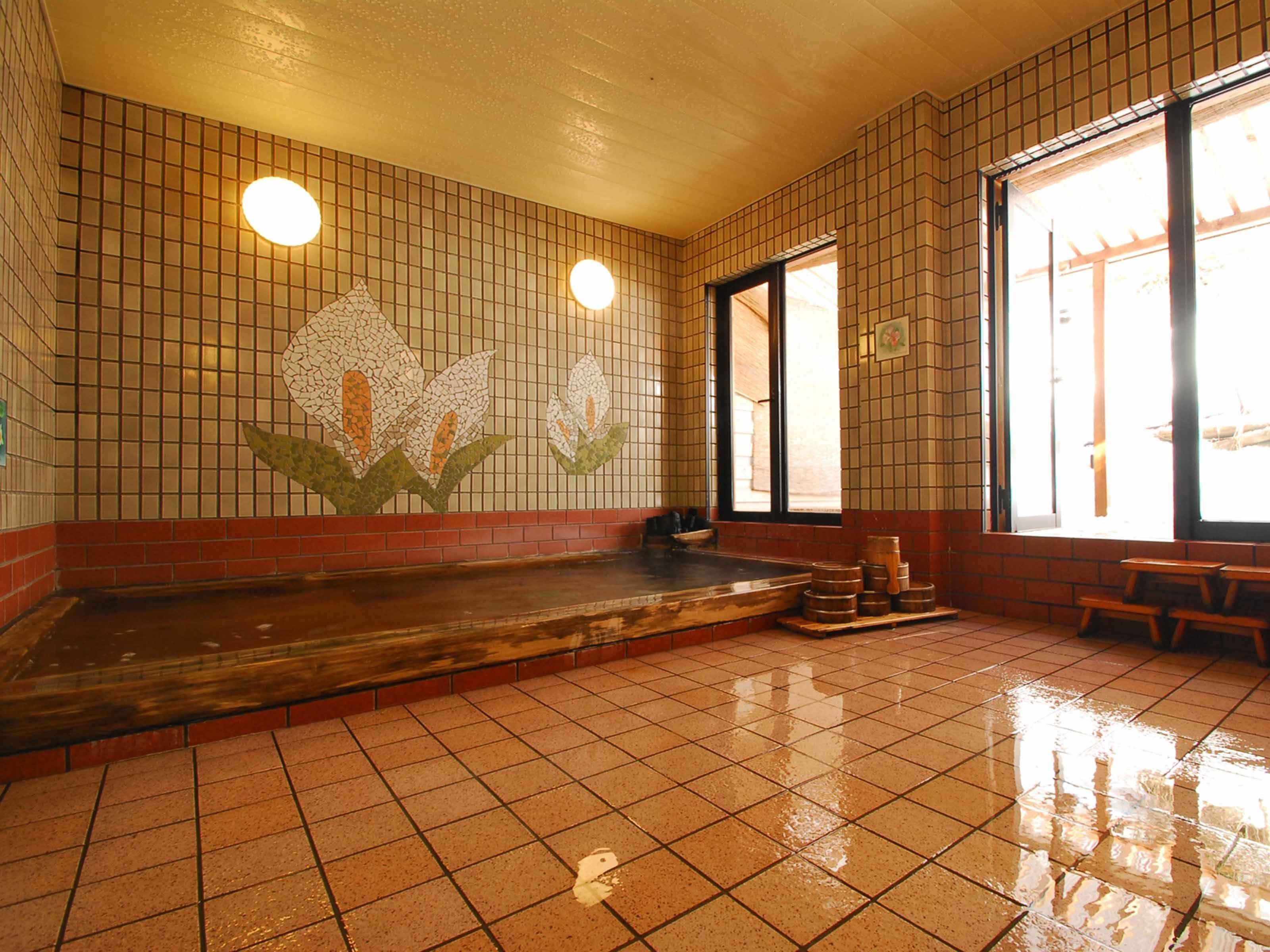 A traditional Japanese onsen with tiled walls, a wooden bench, and a hot spring area.
