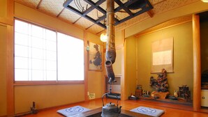 A traditional Japanese room with tatami flooring, a shoji screen, a hanging incense burner, and a small fire pit.
