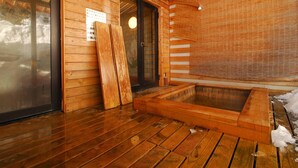 A wooden interior with a hot spring bath, wooden flooring, and a glass door leading outside.