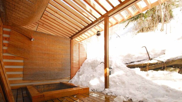 A wooden sauna with a bench and a small hot tub, surrounded by snow.