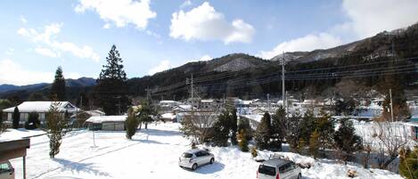 Un estacionamiento cubierto de nieve con varios autos, un edificio de techo plano y montañas al fondo.