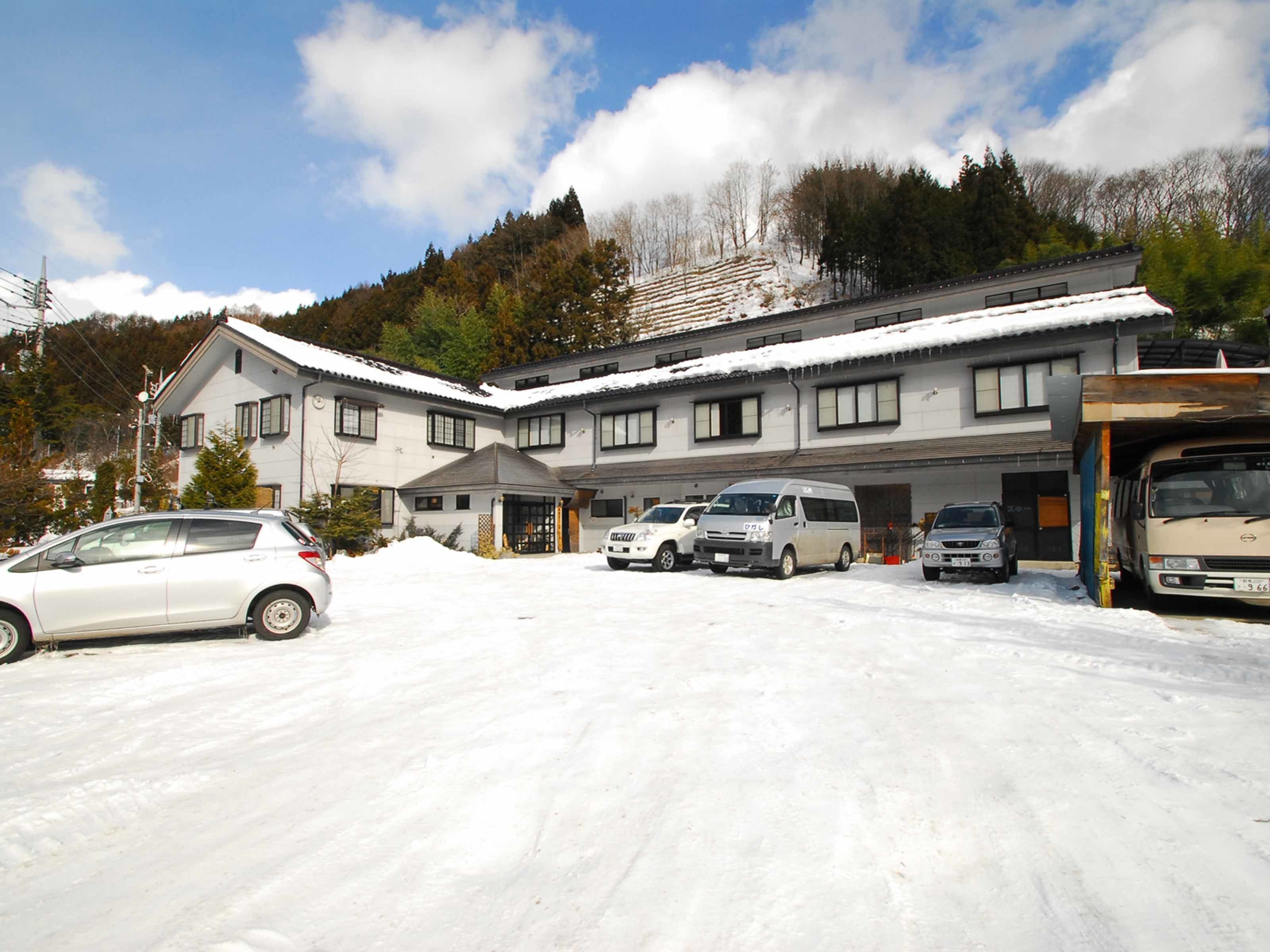 A hotel with multiple buildings, a parking area with several cars, and a snowy landscape.