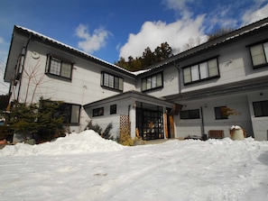 Un bâtiment à deux étages, dont l’entrée est recouverte de neige, et qui dispose d’un petit jardin.