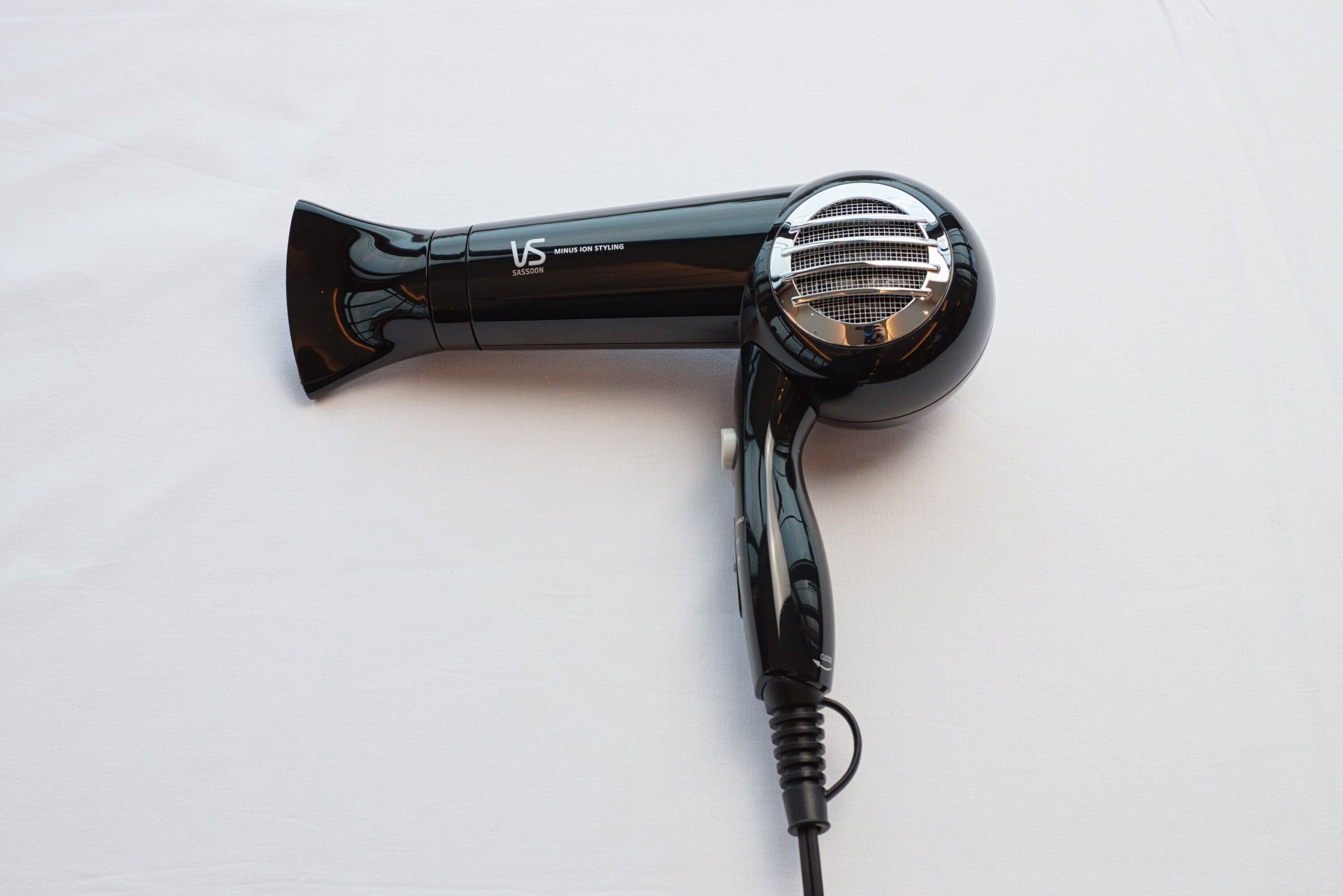 Un sèche-cheveux noir avec un cordon, posé sur une surface blanche.