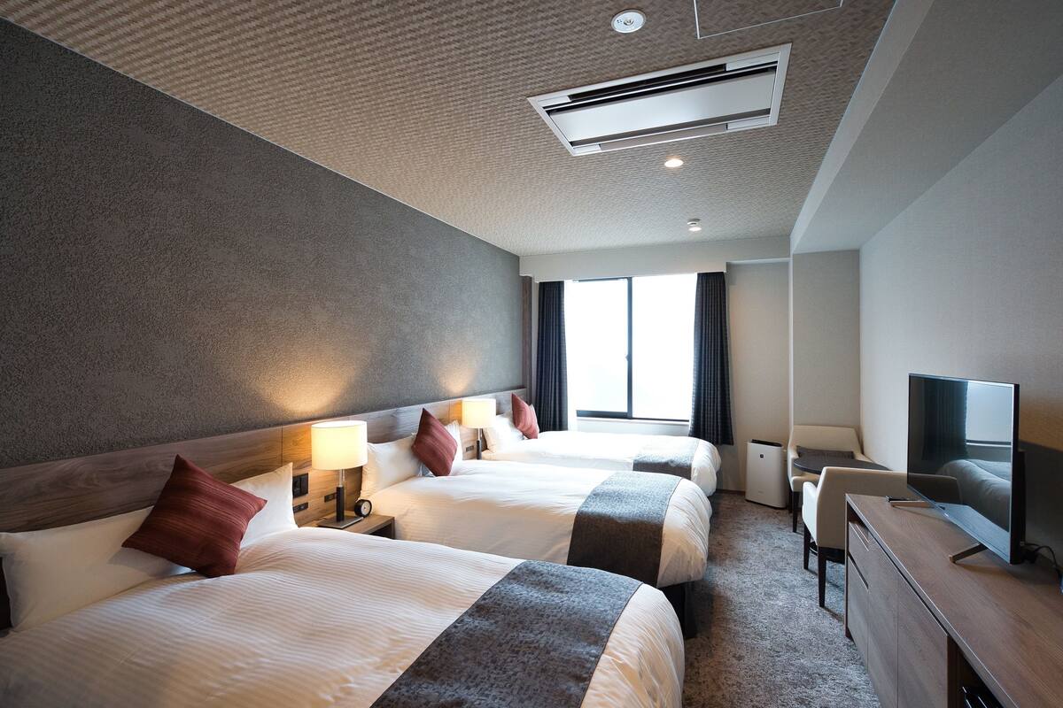 Ein Hotelzimmer mit zwei Betten, einem Schreibtisch, einem Fernseher und einem Fenster mit Vorhängen.