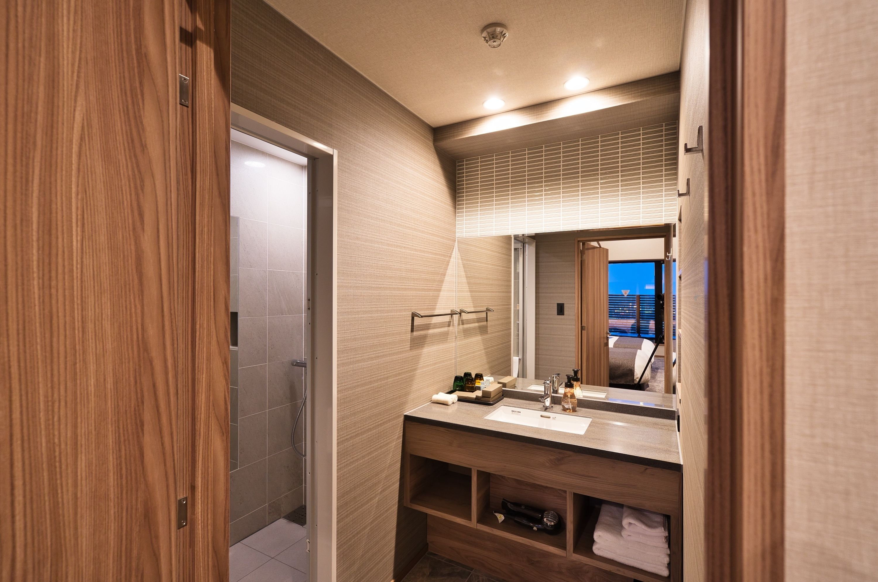 A modern bathroom with a wooden vanity, a large mirror, and a towel rack.