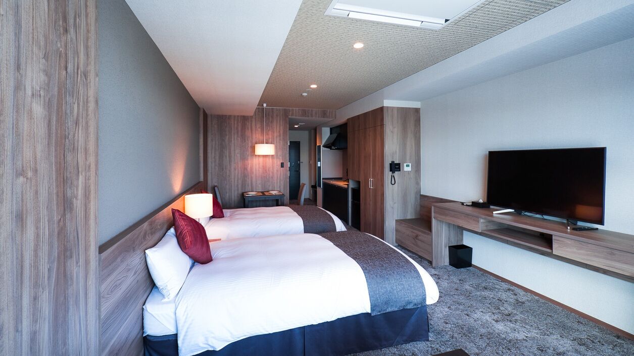 Une chambre d’hôtel avec deux lits, une télévision, un bureau et une kitchenette.