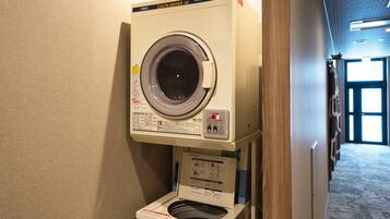 A compact, wall-mounted washer and dryer unit in a hallway with a wooden door frame and a carpeted floor.