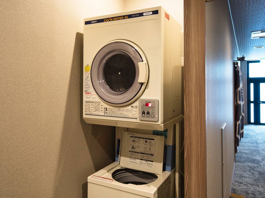 A compact, wall-mounted washer and dryer unit in a hallway with a wooden door frame and a carpeted floor.
