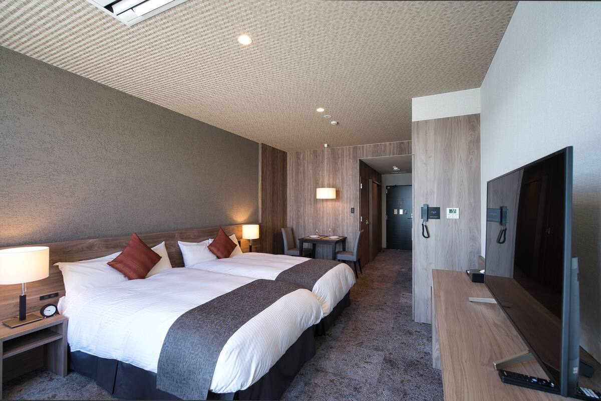 Ein Hotelzimmer mit zwei Betten, einem Schreibtisch, einem Fernseher und einem kleinen Tisch mit Stühlen.
