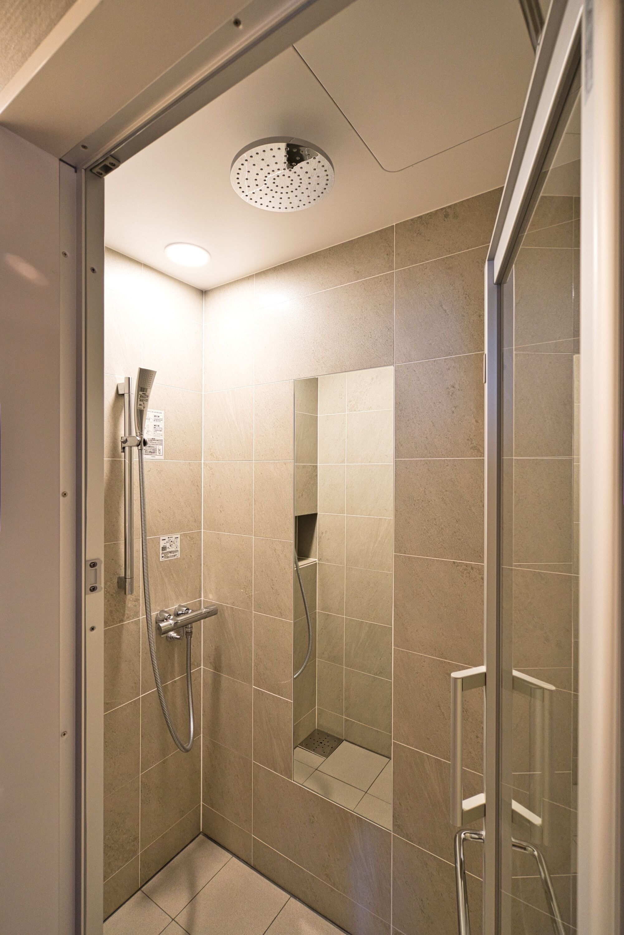 A modern shower with a glass door, a handheld showerhead, and a wall-mounted faucet.