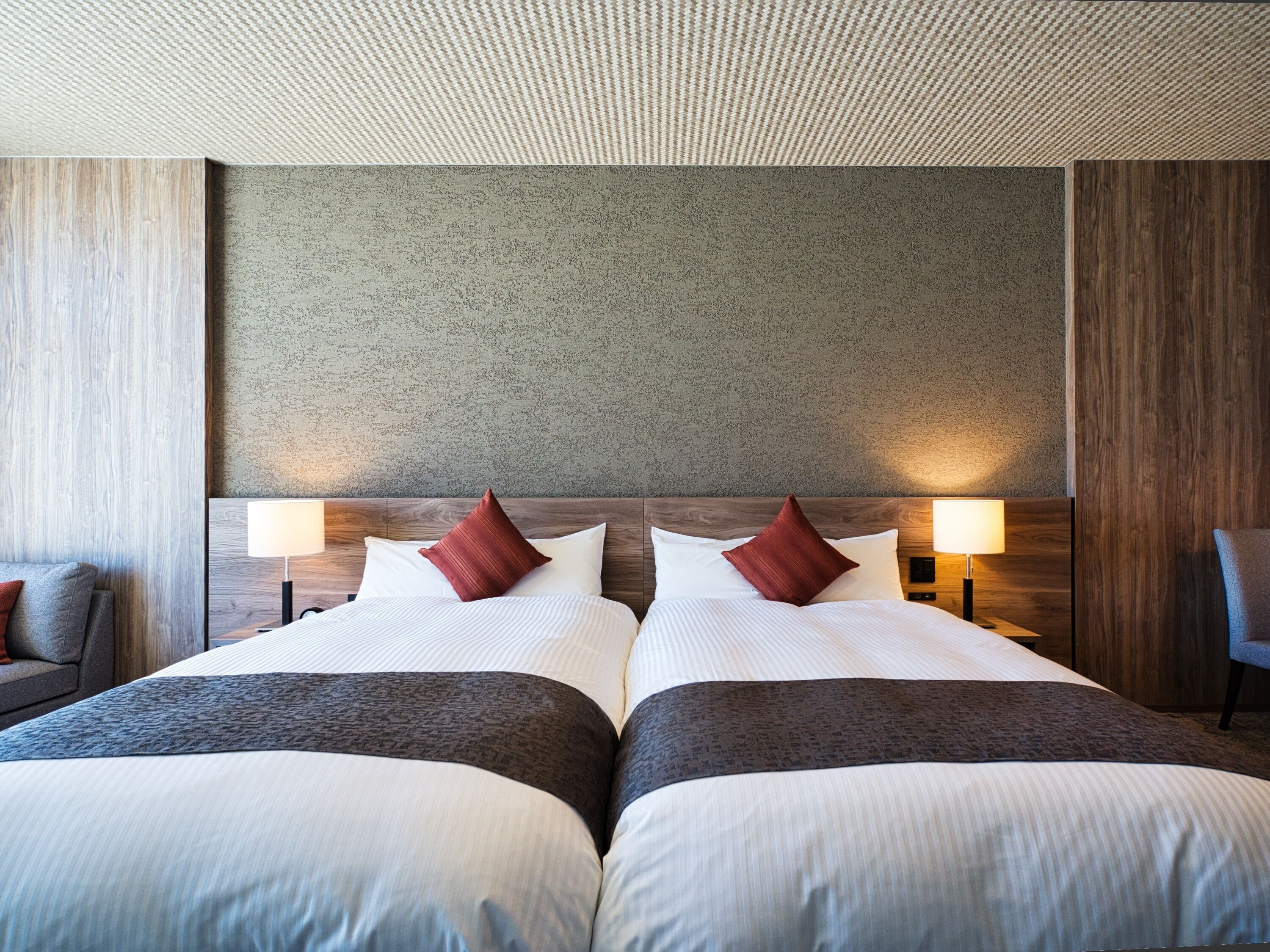 Une chambre d’hôtel avec deux lits, une tête de lit en bois, un mur à texture et deux lampes de chevet.