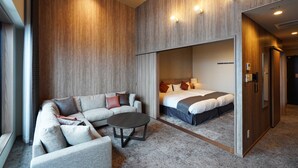 Moderni hotellihuone, jossa on sohva, pyöreä sohvapöytä ja sängyssä pääty.