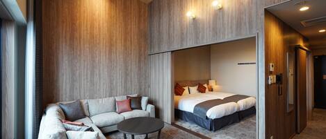 A modern hotel room with a sofa, a round coffee table, and a bed with a headboard.