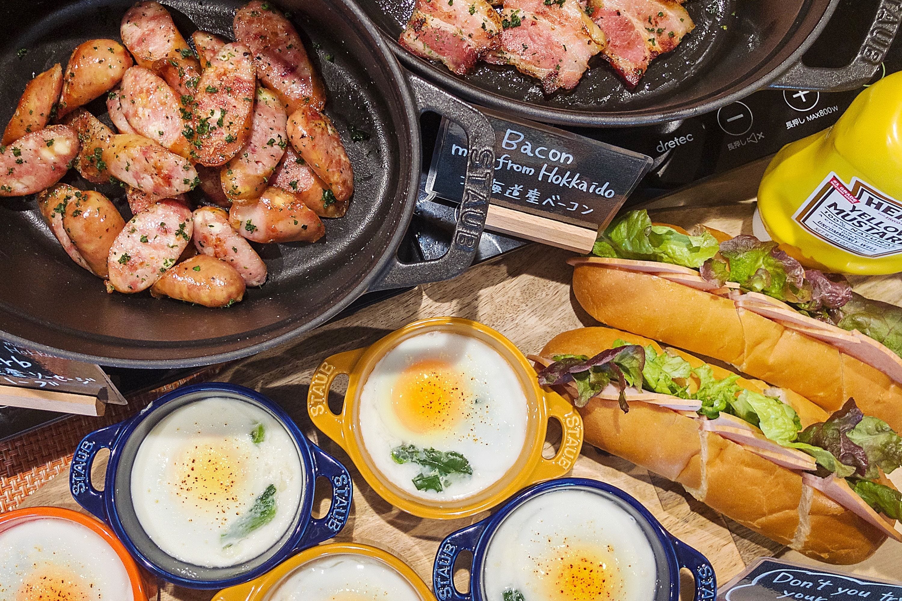 Una mesa de desayuno con tocino, salchichas, huevos y sándwiches.