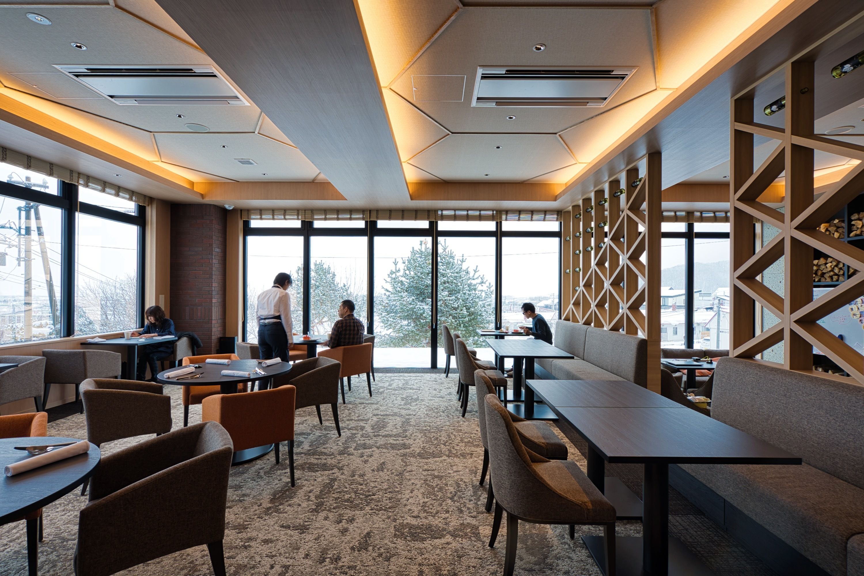 A modern dining area with tables and chairs, large windows, and a view of the outdoors.