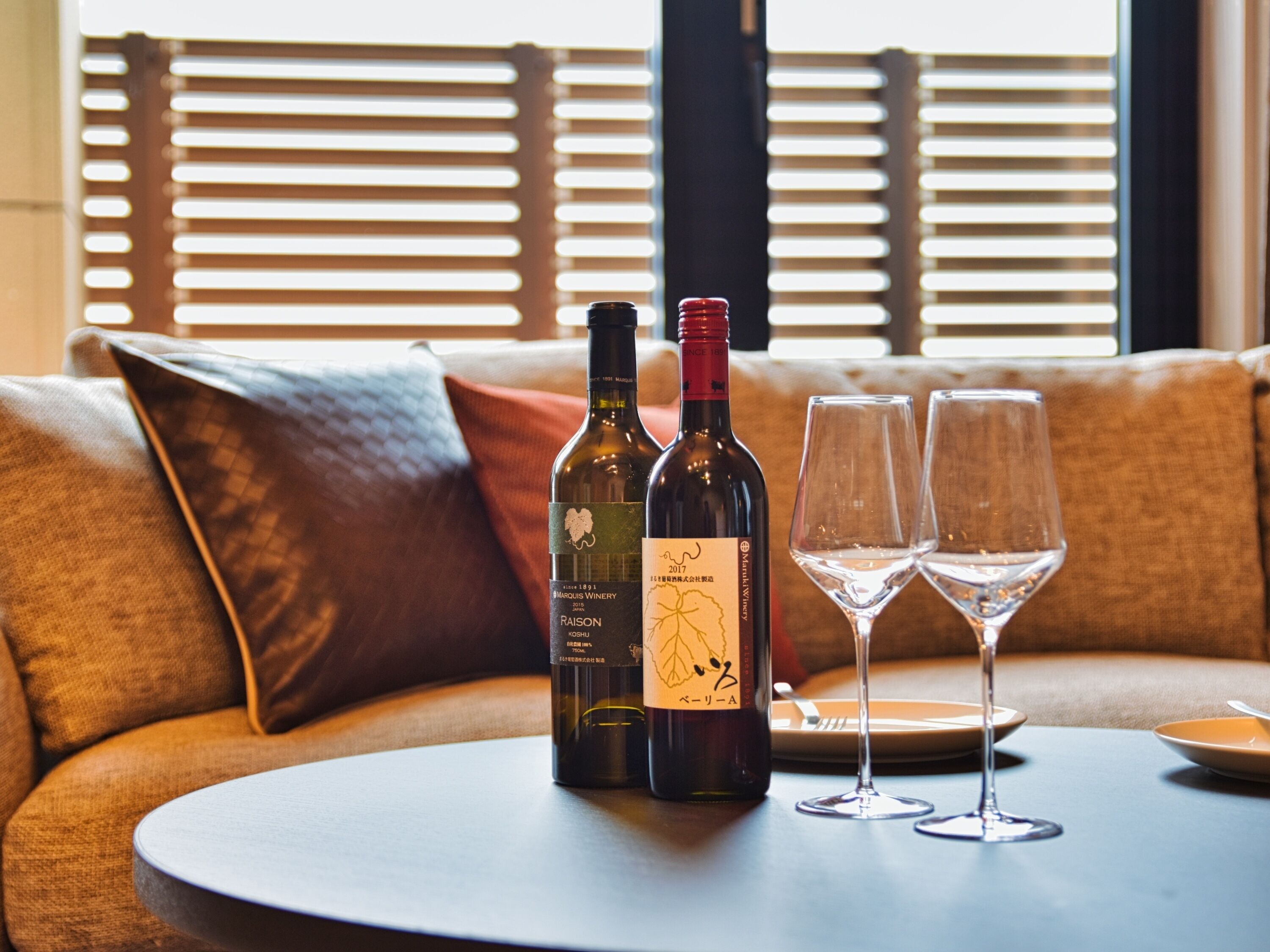 A round table with a bottle of wine and two empty wine glasses on a sofa.