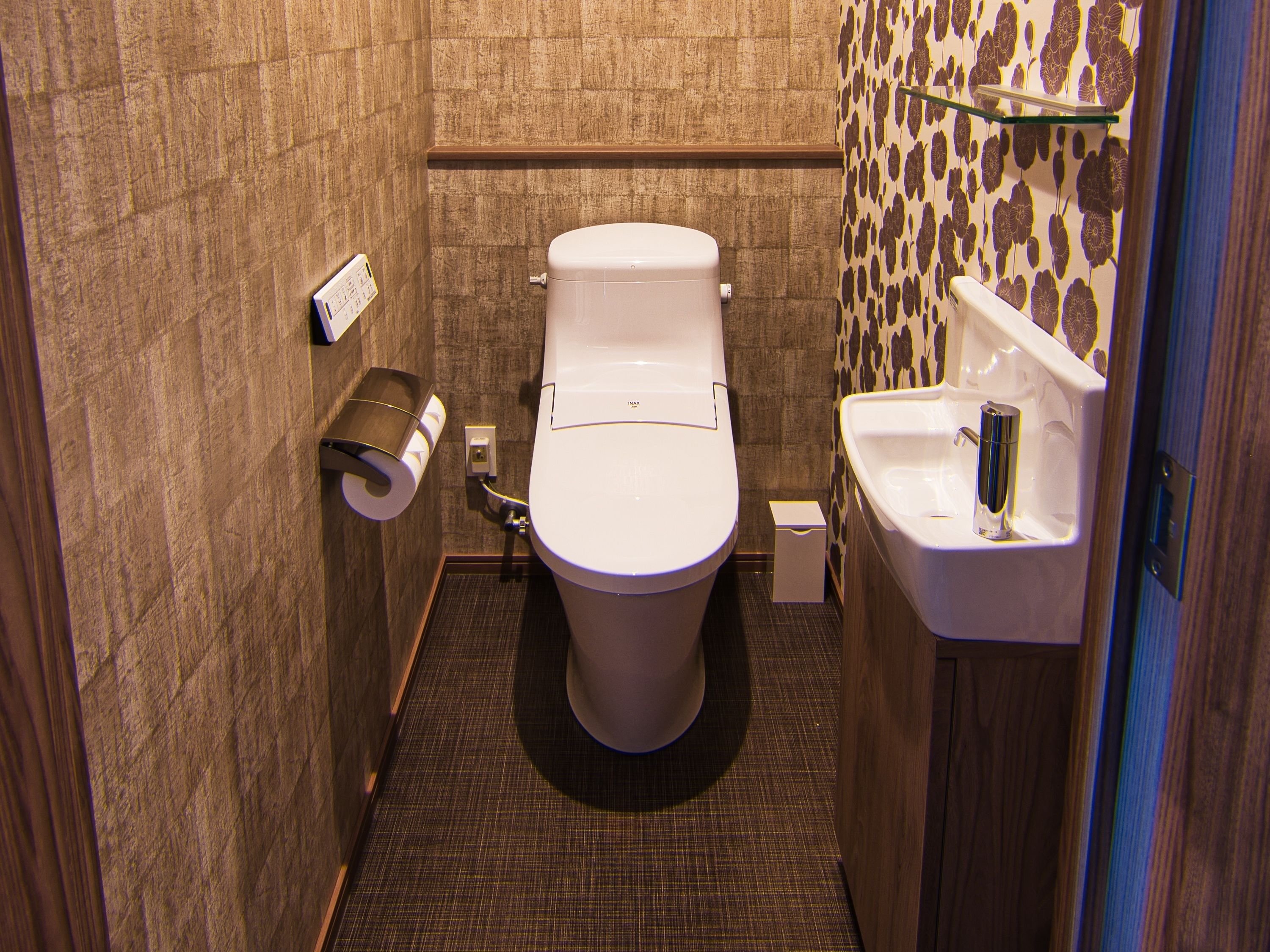 A compact bathroom with a toilet, a paper towel dispenser, a small sink, and a shower area.