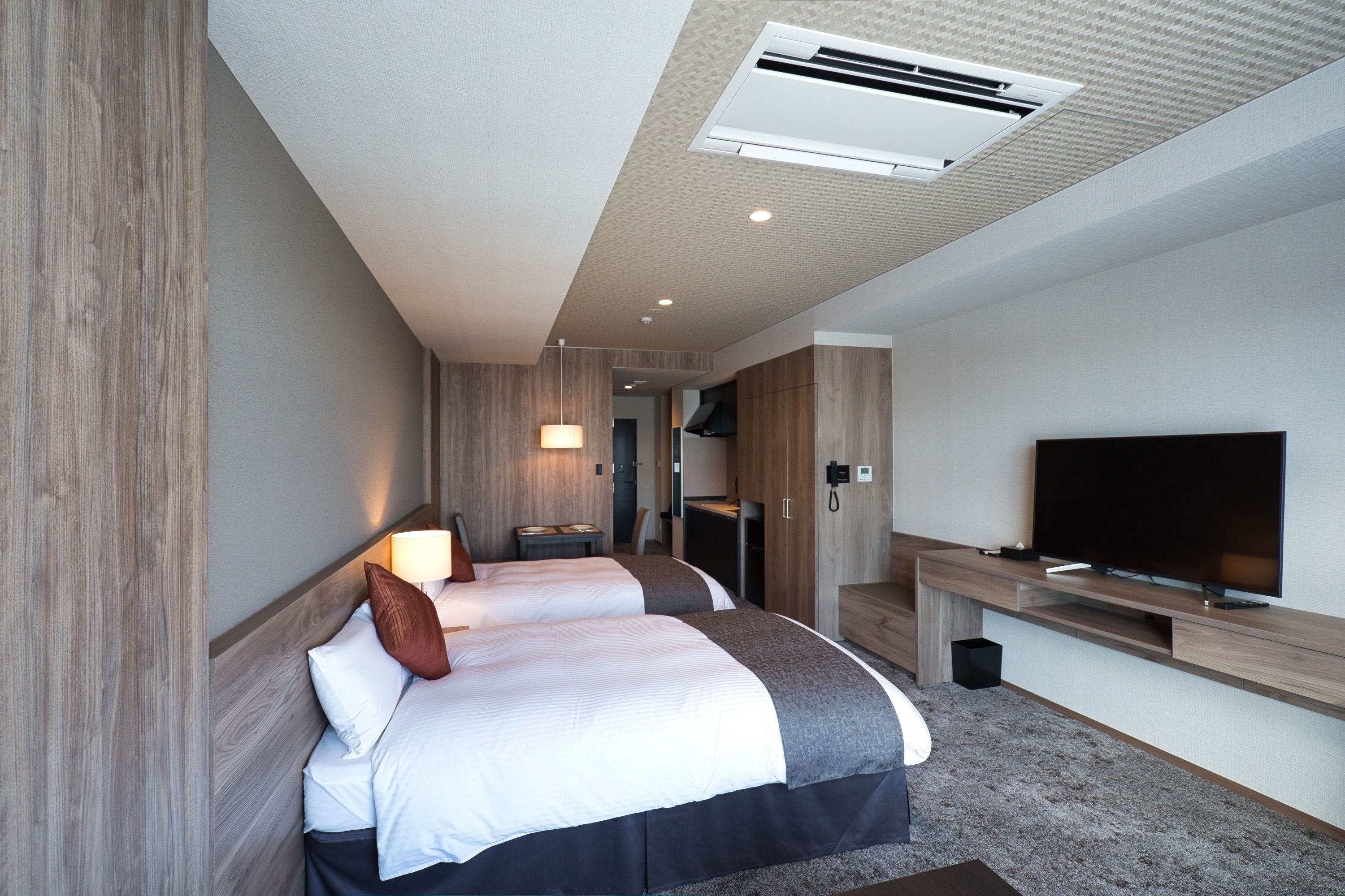 A modern hotel room with two beds, a flat-screen TV, a desk, and a built-in wardrobe.