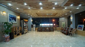 A spacious lobby with a wooden ceiling, a reception desk, comfortable seating, and a large window offering a night view. - Raum Hotel (Jeju City)