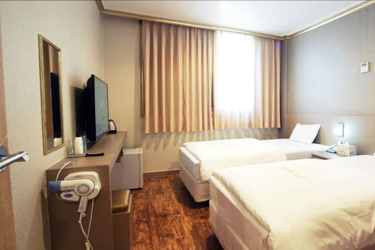 A hotel room with two beds, a TV, a hairdryer, and a window with curtains.