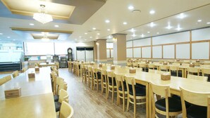 A spacious dining area with multiple tables and chairs, a chandelier, and a large window. - Raum Hotel (Jeju City)