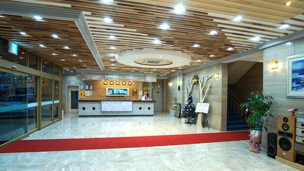 A hotel reception area with a wooden ceiling, a reception desk, a digital information board, and a Christmas tree. - Raum Hotel (Jeju City)