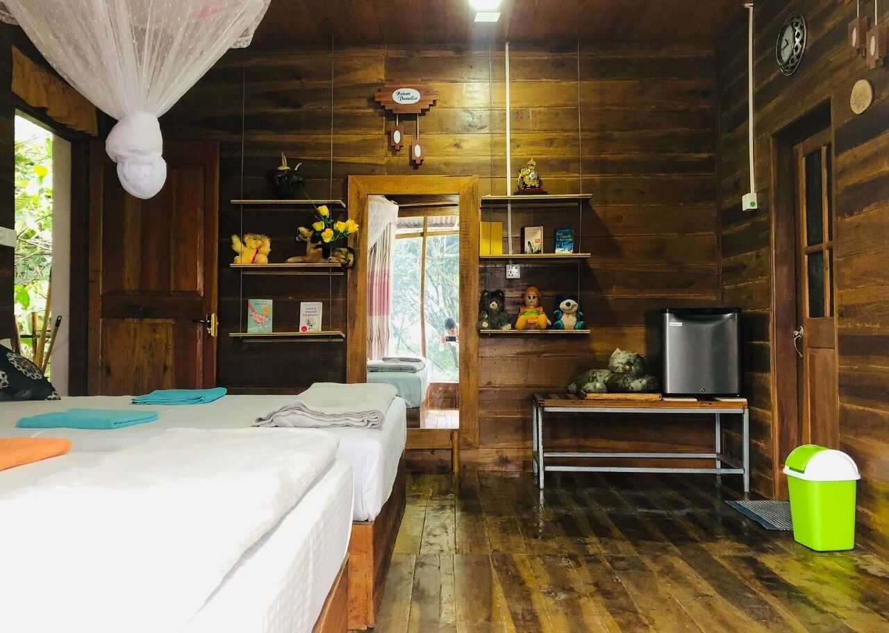 A wooden cabin room with two beds, a television, a small table, and a trash bin.