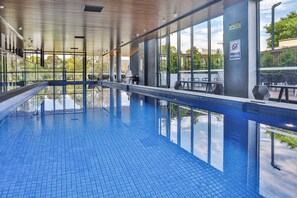 A modern indoor swimming pool with clear glass walls, a tiled floor, and a wooden ceiling. - Melbourne Knox Central Apartment Hotel (Wantirna South)
