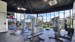 A gym with various exercise machines, large windows, and a view of the outdoors. - Melbourne Knox Central Apartment Hotel (Wantirna South)