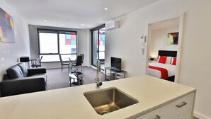 A modern hotel room with a kitchenette, a dining area, and a bed with red bedding. - Melbourne Knox Central Apartment Hotel (Wantirna South)