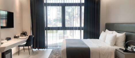 Una habitación de hotel moderna con una cama grande, un escritorio, un televisor y vistas a la ciudad a través de amplias ventanas.