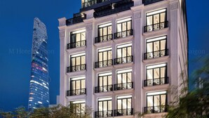 Un hotel de varios pisos con un cartel iluminado llamativo, un edificio de cristal moderno al fondo y un área de entrada bien iluminada.