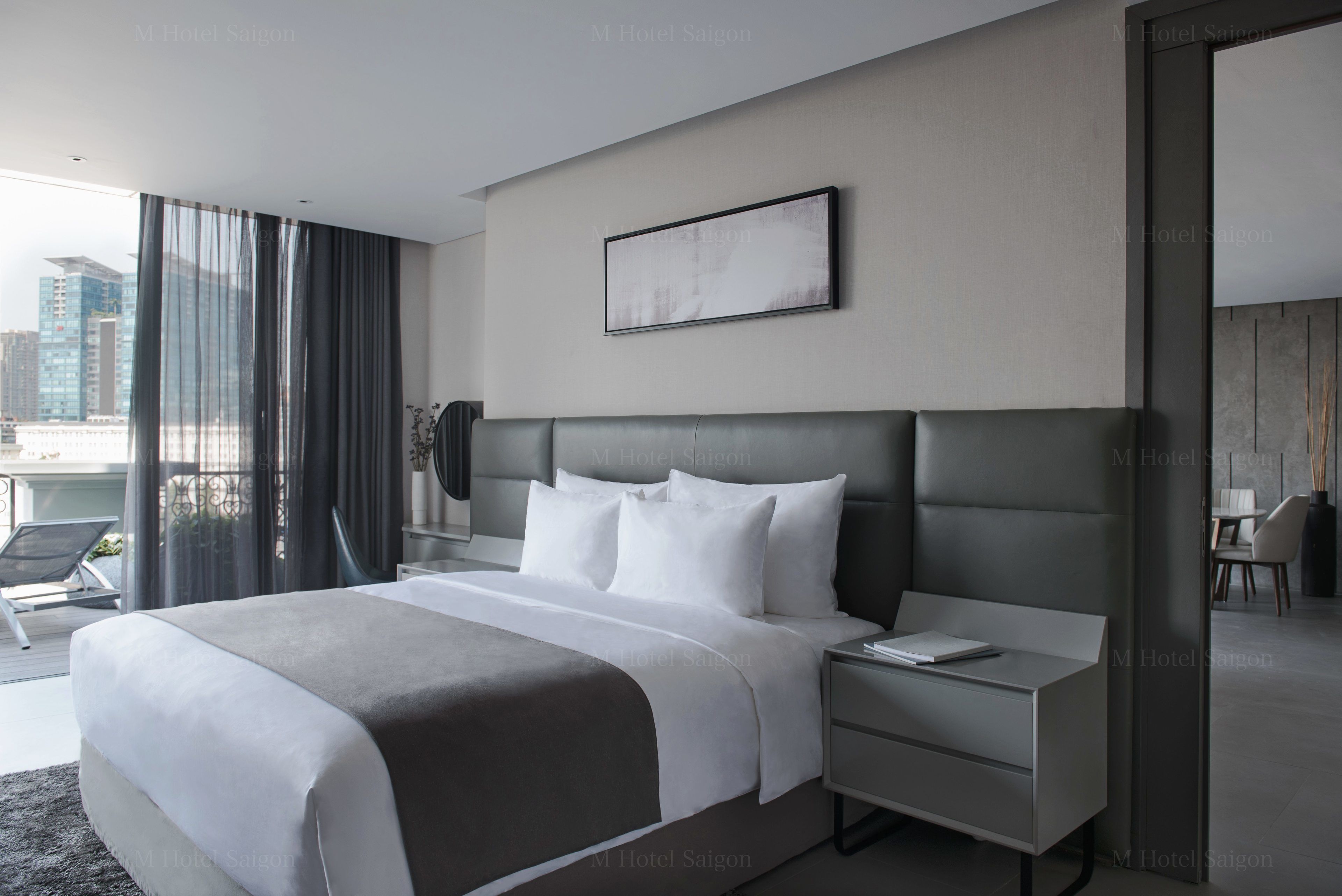 A modern hotel room with a large bed, a bedside table, a chair, and a view of the city.