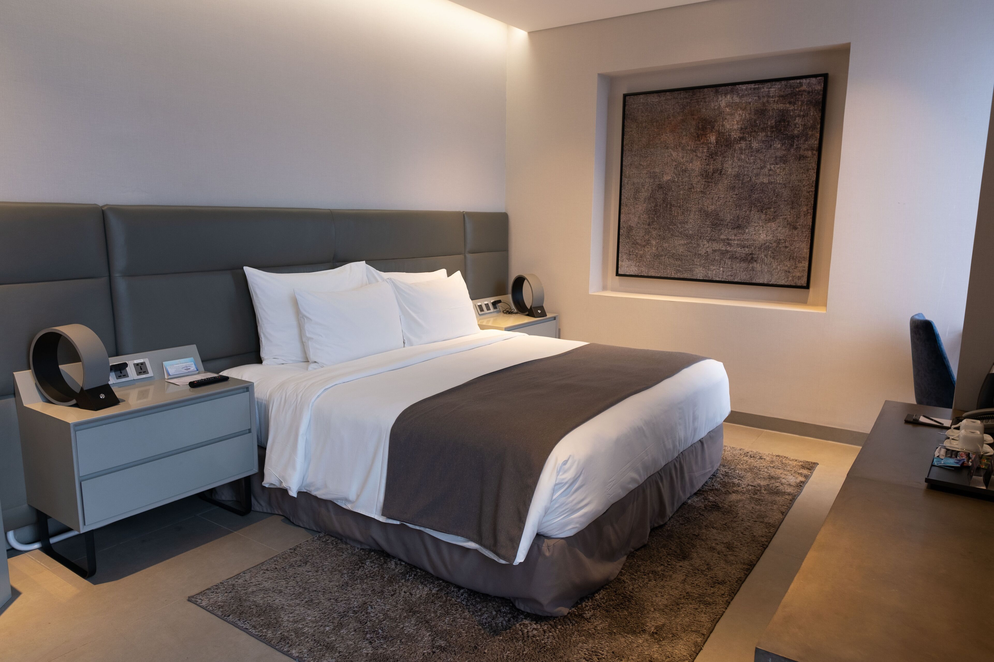 A modern bedroom with a large bed, bedside tables, a desk, and a framed artwork on the wall.