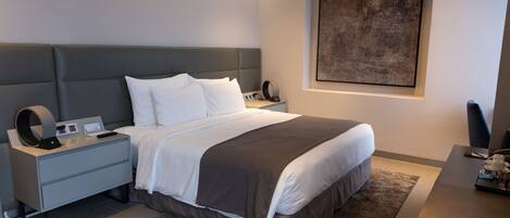 A modern bedroom with a large bed, bedside tables, a desk, and a framed artwork on the wall.