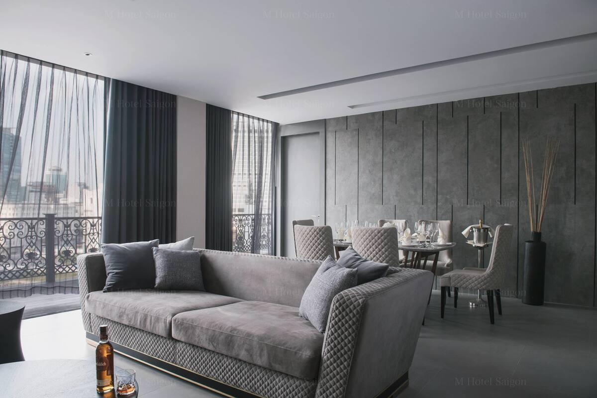 A modern hotel room with a grey sofa, dining table, and chairs.
