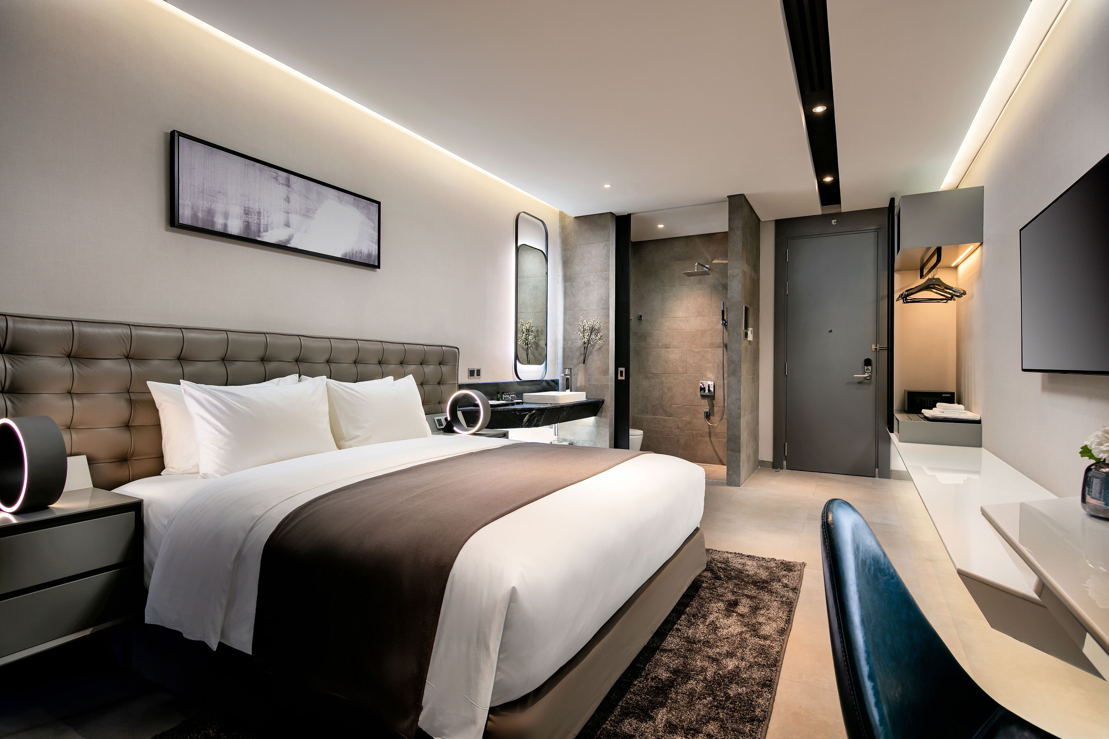 Un dormitorio moderno con una cama grande, mesitas de noche, un escritorio y un espejo.