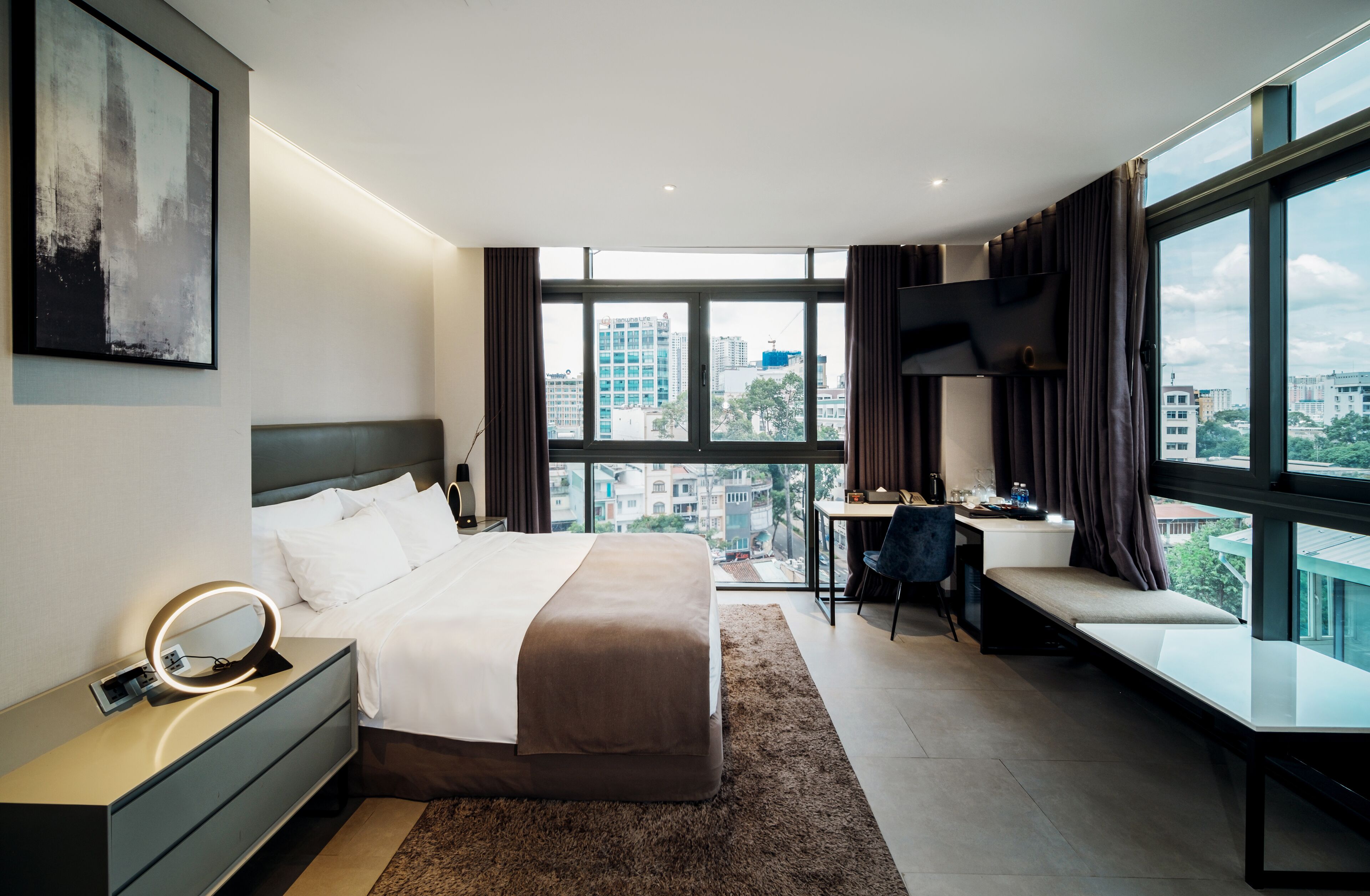 A modern hotel room with a large bed, a desk, and a view of the city.