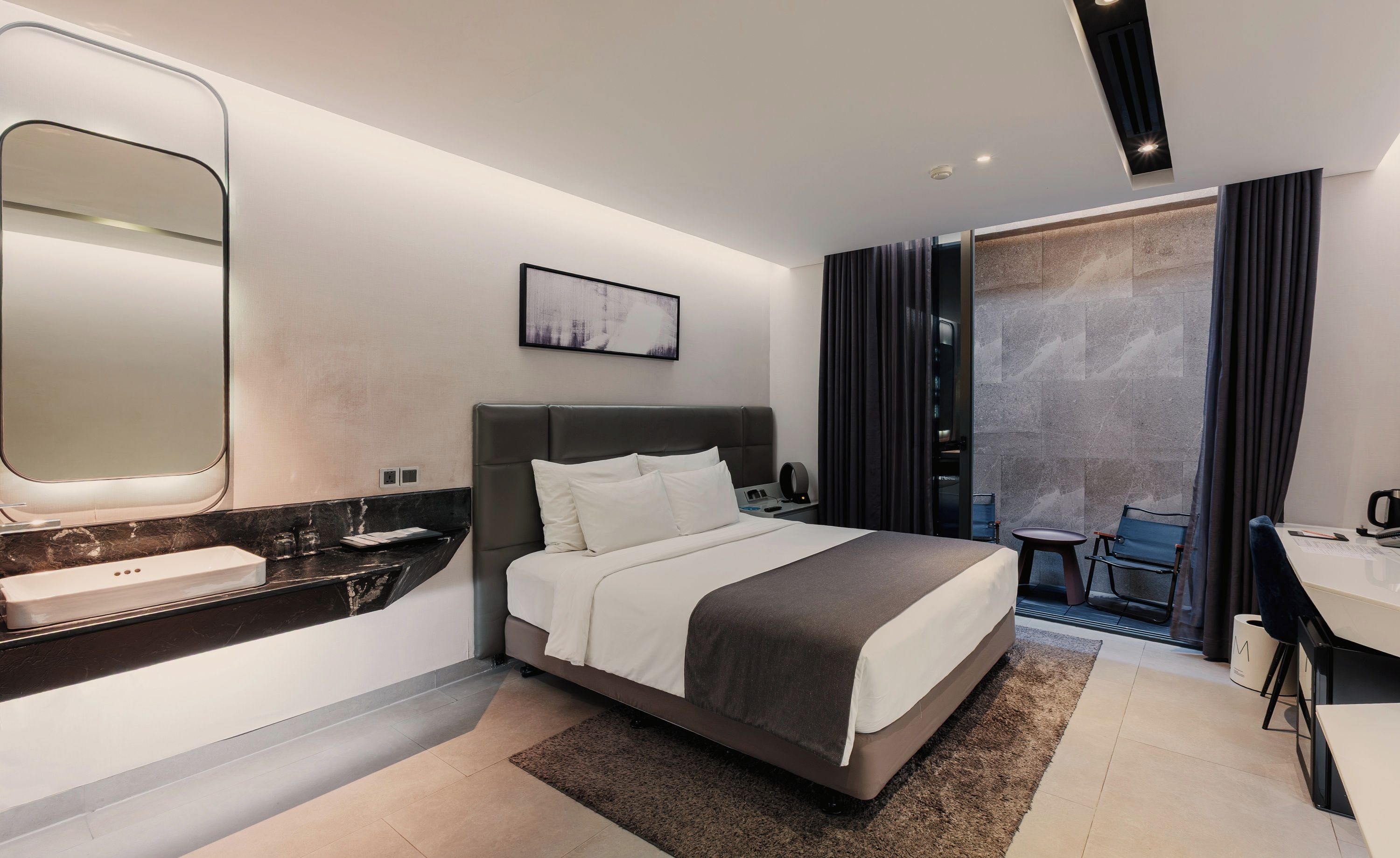 Een moderne hotelkamer met een bed, nachtkastje en een grote spiegel.