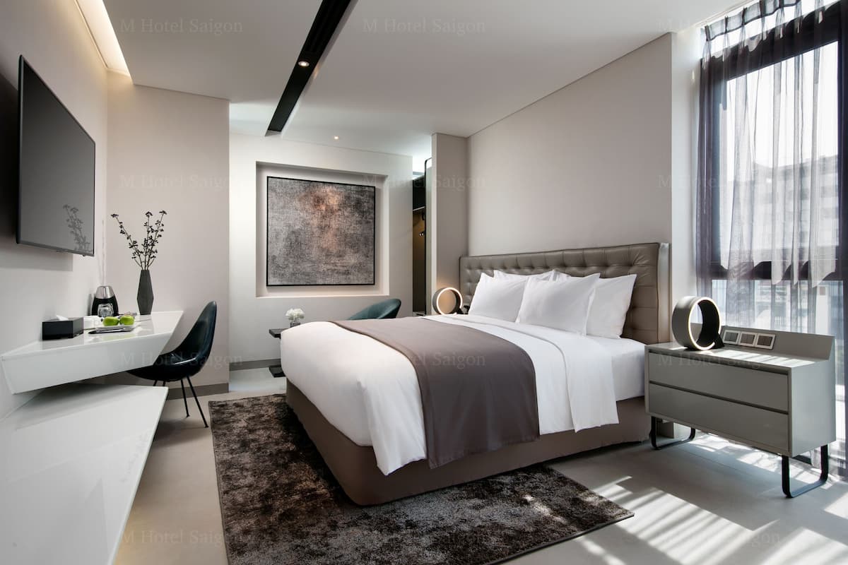 A modern bedroom with a large bed, bedside tables, a desk, and a large window.