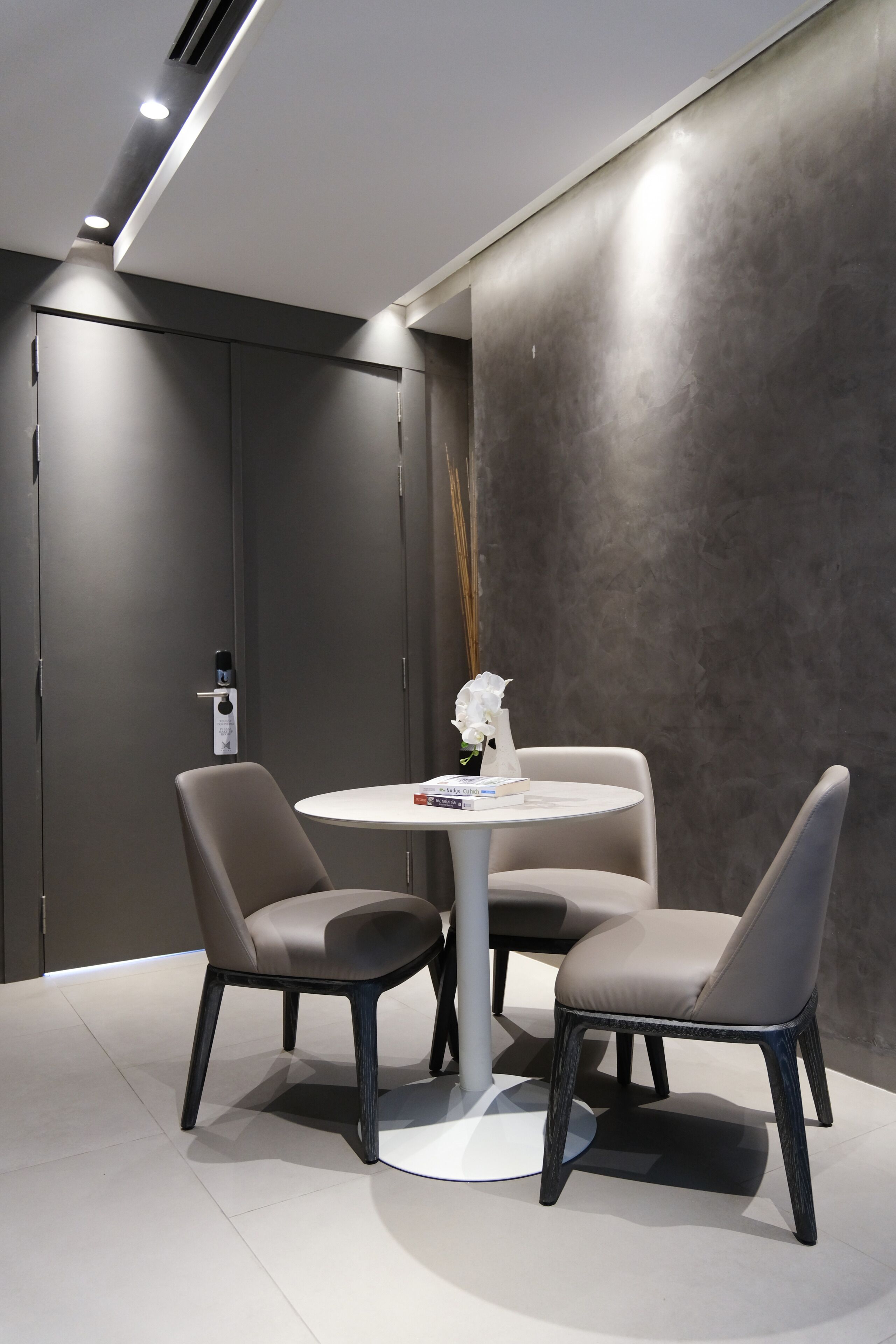 A modern room with a round table and two chairs, a vase with a white flower, and a door with a lock.