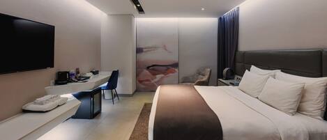A modern hotel room with a large bed, a desk with a flat-screen TV, a chair, and a wall-mounted TV.