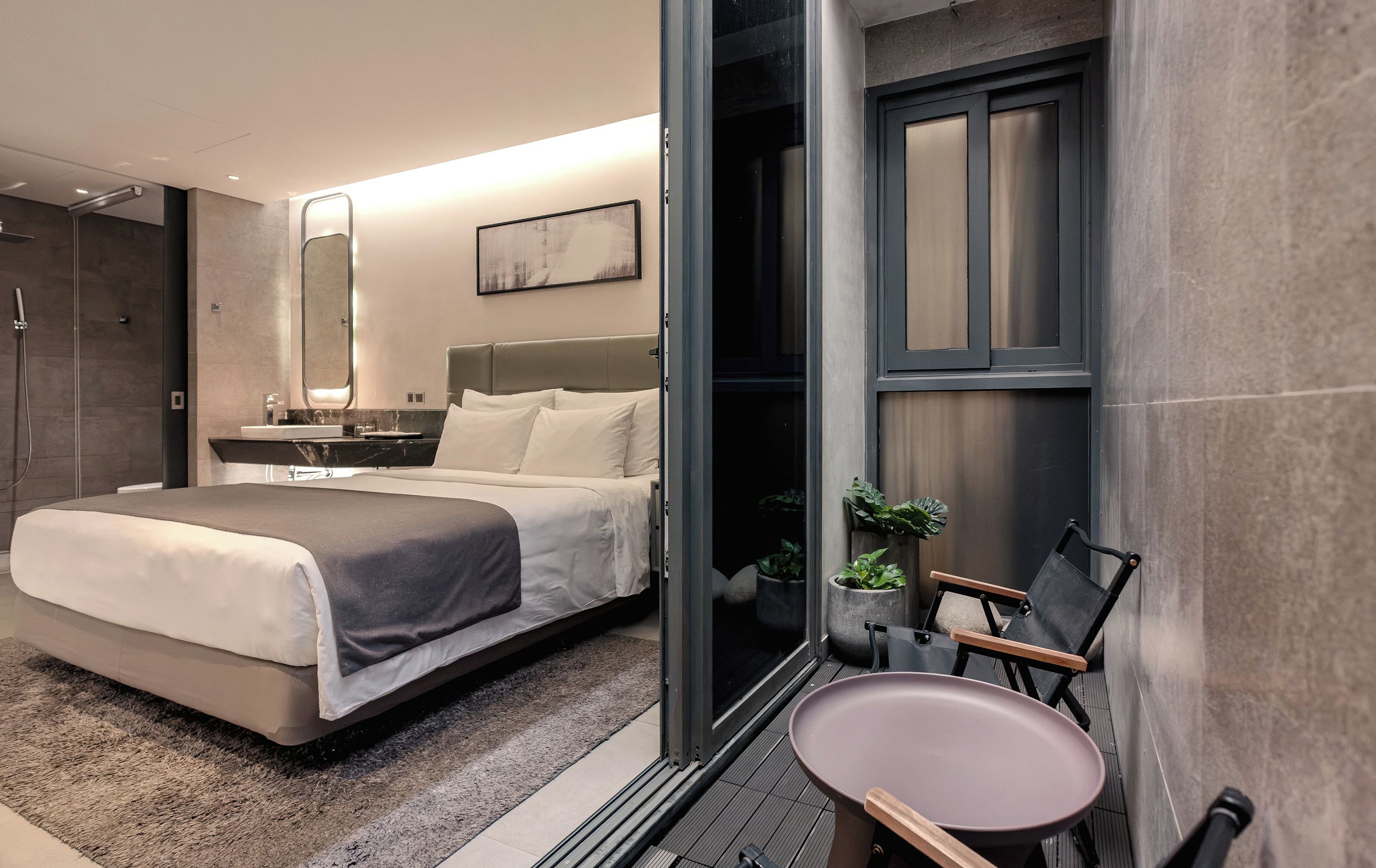 Una habitación de hotel moderna con cama, mesita de noche, espejo y puerta que da a un balcón.